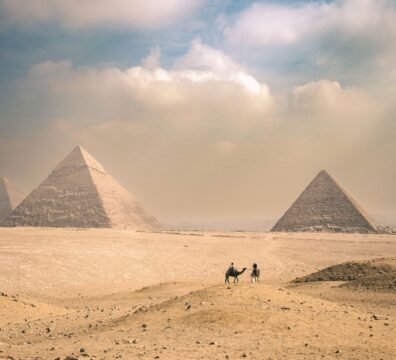 Explore the majestic Pyramids of Giza under a sunny sky with distant travelers on camels.